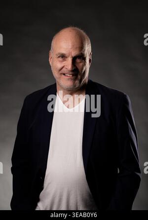 Uomo calvo sorridente, con blazer scuro e t shirt bianca per un ritratto in studio Foto Stock