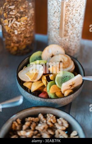 Le fette di frutta fresca riempiono un recipiente rustico. Colori vivaci mettono in risalto l'assortimento. Le noci aggiungono una consistenza naturale in un altro recipiente. I barattoli di muesli si alzano dolcemente Foto Stock