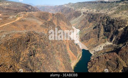 Vista aerea dell'aspro canyon del deserto con ripide scogliere rocciose e un tortuoso bacino idrico sottostante sotto la luce del sole, che mostra un paesaggio arido e remoto Foto Stock
