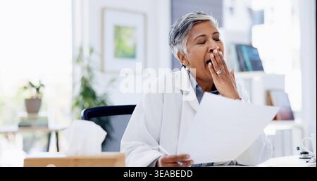Dottore, scartoffie e donna con sbadigliato in ufficio per l'amministratore, stanchezza e sfinito con lavoro medico. Persona matura, stanca e documenti per l'assistenza sanitaria Foto Stock