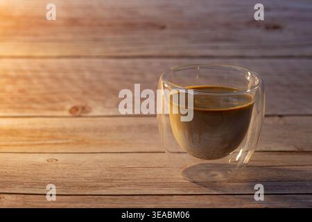 Vista laterale del caffè sporco a strati in vetro a doppia parete su un tavolo in legno rustico. Calda luce solare mattutina d'oro con spazio per fotocopie. Foto Stock