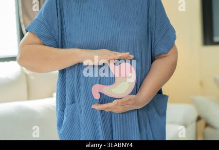 Donna anziana con stomaco che sente dolore o gastrico mentre è in piedi a casa. Senior che soffre di problemi di digestione o reflusso acido. Foto Stock