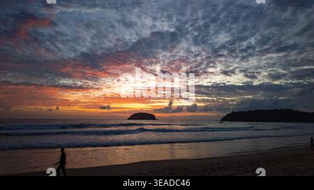 Una vista mozzafiato del sole che tramonta sull'oceano, che proietta calde sfumature dorate sulle onde e le nuvole mentre la gente si gode la tranquilla costa. Foto Stock