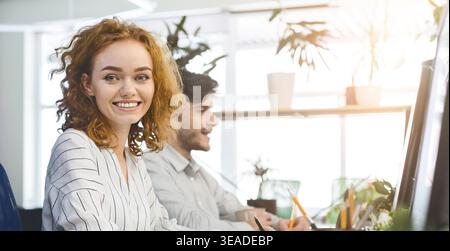 Carino redhead donna in office, sorridente in telecamera Foto Stock