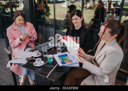 Tre colleghi donne che tengono una riunione di lavoro e esaminano i rapporti al tavolo di un bar Foto Stock