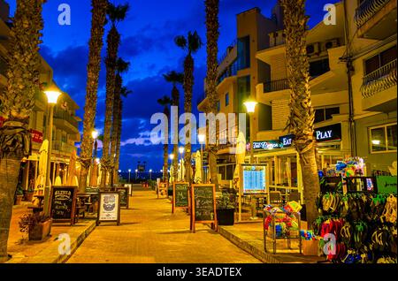 BUGIBBA, Malta - 14 giugno 2018: Serata Bay quadrato con una vista sulle bancarelle di souvenir, popolari cafè, ristoranti e palm vicolo lungo la zona dello shopping, Foto Stock