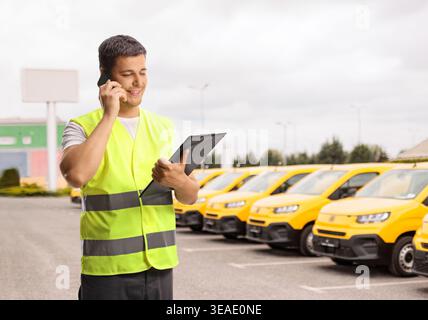 Addetto all'assistenza stradale davanti a furgoni gialli in possesso di un documento ed effettuando una telefonata Foto Stock