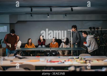 Studenti e amici giocano a ping pong e socializzano in una rilassata sala comune interna Foto Stock