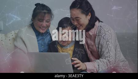 Guardare la famiglia di più generazioni che si appoggia sul divano del soggiorno, utilizzando un computer portatile color argento con sovrapposizione di mappe Foto Stock
