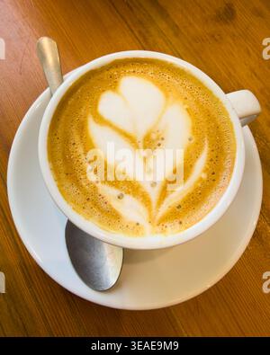 Design floreale sulla superficie del caffè in tazza bianca con sppoon e piattino su superficie in legno Foto Stock