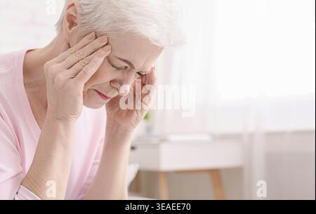 Donna anziana che ha mal di testa e tocca i templi Foto Stock