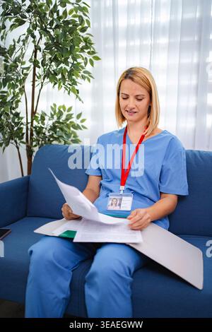 Medico donna che esamina le cartelle cliniche mentre si siede sul divano in ospedale Foto Stock