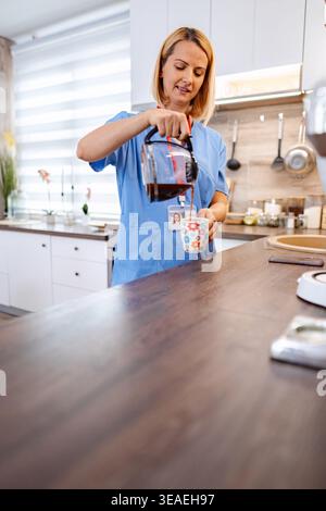 Infermiere che versa caffè in cucina durante la pausa di lavoro Foto Stock