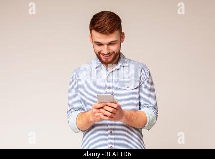 Giovane uomo absorbedly la messaggistica di testo sul suo cellulare Foto Stock