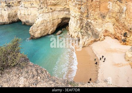 Vista dall'alto di una spiaggia di sabbia isolata e di una grotta sul mare circondata da scogliere calcaree sulla costa dell'Algarve, in Portogallo, con acqua turchese e piccole Foto Stock