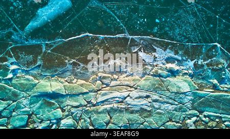 Trame di ghiaccio e crepe aeree sul lago ghiacciato in inverno dall'alto verso il basso Foto Stock