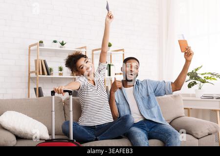 Viaggiatori entusiasti che celebrano il loro prossimo viaggio con biglietti e bagagli in un accogliente soggiorno Foto Stock