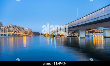 L'Inner Harbour Bridge di Copenaghen si erge sull'acqua mentre gli edifici si riflettono sulla superficie tranquilla. Il cielo si oscura, creando una scena di vita cittadina vicino al lungomare. Foto Stock