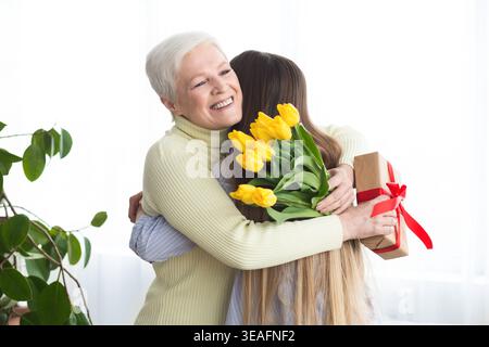Figlia che dà fiori e regalo a sua madre Foto Stock
