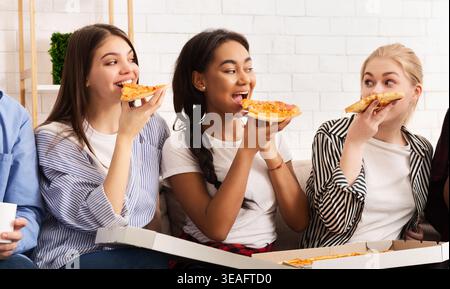 Amici che amano la pizza insieme in un accogliente salotto Foto Stock