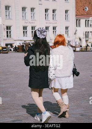 Due giovani donne camminano attraverso la Piazza del Municipio nella città vecchia di Tallinn in una giornata di primavera soleggiata, vista da dietro Foto Stock