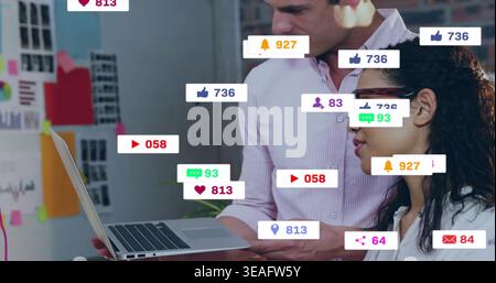 Tenendo in mano un laptop, i colleghi indossano abiti da ufficio appoggiati in ufficio, visualizzando icone e appunti sui social network Foto Stock