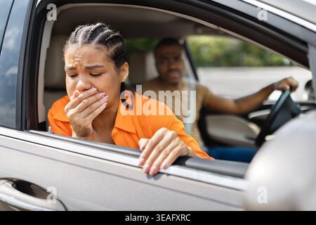 Giovane donna nera che sente il mal di testa che si sporge dal finestrino dell'auto aperto Foto Stock