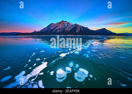 Bolle di metano nel lago ghiacciato e montagna al tramonto in inverno Foto Stock
