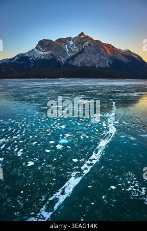 Ghiacciate sul lago ghiacciato e montagna innevata all'alba in inverno Foto Stock