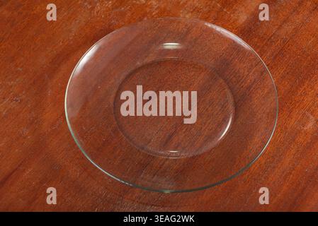 L'asta è caratterizzata da una lastra di vetro trasparente contro la superficie in legno. L'illuminazione evidenzia la trasparenza della piastra. Sfondo ricco di texture in legno scuro. Ideale f Foto Stock