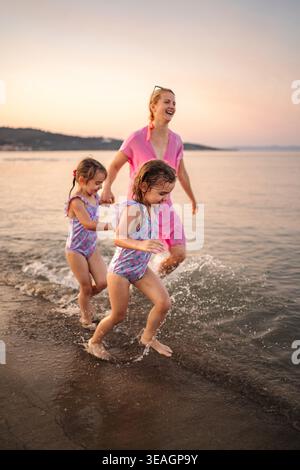Madre e figlie si divertono a correre sulla spiaggia al tramonto in Grecia Foto Stock