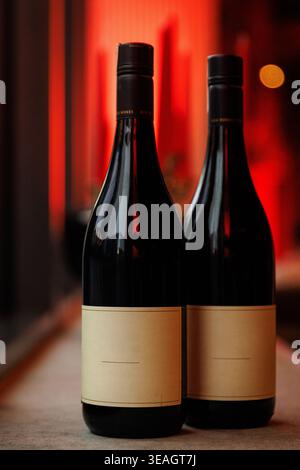 Un paio di bottiglie di vino di vetro scuro si stagliano su un bancone su un caldo sfondo rosso con luci bokeh. Foto Stock