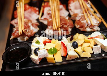 Un vassoio di ristorazione gourmet con prosciutto a fette, prosciutto, cubetti di formaggio, fragole e grissini croccanti. Foto Stock