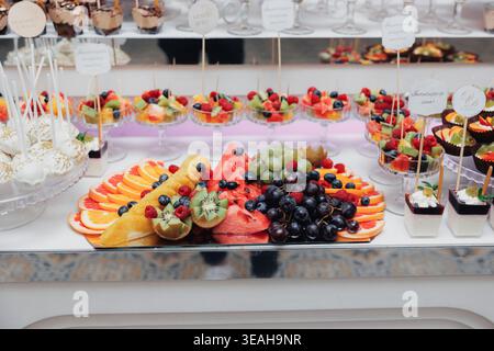 Piatto di frutta colorata e dessert con spiedini di agrumi, frutti di bosco e tropicali a fette disposti su un banco di marmo, Bright Summer Vibe per brunch Foto Stock