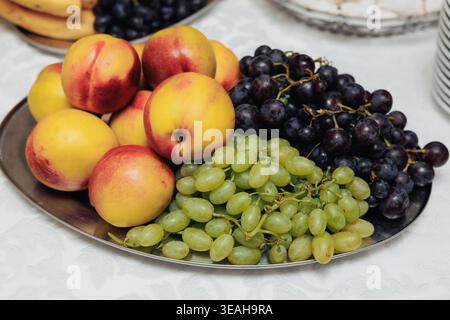 Pesche mature e uva assortite per un elegante brunch. Vivace frutta di stagione, tra cui pesche e uva, splendidamente allestita Foto Stock