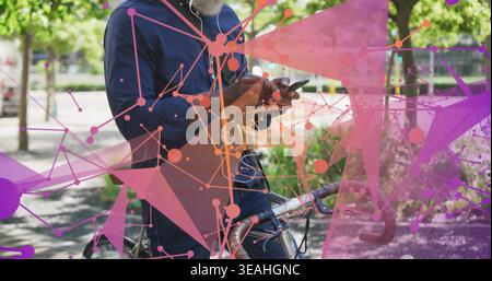 Controllare lo smartphone, l'uomo con la camicia navy, i jeans che si trovano al parco in bicicletta con auricolari e mascherina Foto Stock
