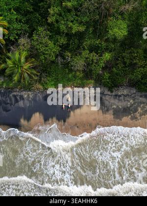 Vista aerea di due persone sdraiate su una spiaggia sabbiosa con onde che si infrangono e lussureggiante giungla tropicale di Palomino, la Guajira, Colombia. Foto Stock
