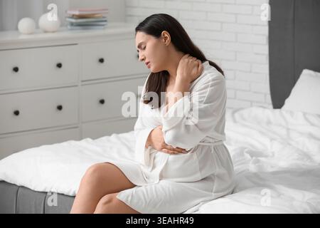 Donna incinta in accappatoio soffre di dolore al collo sul letto a casa Foto Stock