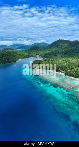 Vista aerea di We Island con acque turchesi, un molo di legno e lussureggianti colline tropicali sotto un cielo nuvoloso, Sabang City, Aceh, Indonesia. Foto Stock