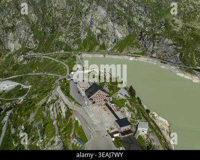 Vista aerea del passo Grimsel con lo storico edificio in pietra che si affaccia sul lago alpino turchese e sulle tortuose strade di montagna di Obergoms, Virginia Foto Stock