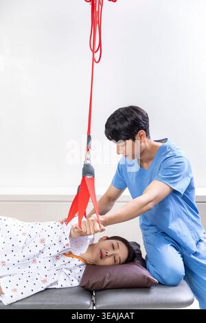 Un paziente giovane è sdraiato su un tavolo e riceve un trattamento di fisioterapia da un terapeuta che utilizza una cinghia rossa per facilitare la mobilità del paziente. Foto Stock