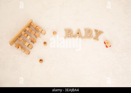 Un abaco di legno e blocchi sono disposti su una superficie bianca accanto alla parola "BABY" in lettere di legno. Foto Stock