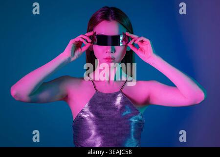 Una giovane donna che indossa occhiali VR futuristici in un ambiente buio e illuminato al neon. Foto Stock