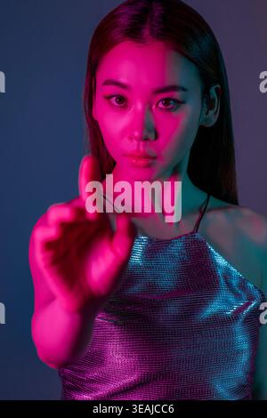 Una giovane donna con un vestito d'argento si trova in una stanza buia, la sua mano alzata in un gesto di avvertimento. Foto Stock