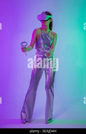 Una giovane donna che indossa un visore VR e tiene in mano i controller, in una stanza futuristica e illuminata al neon. Foto Stock
