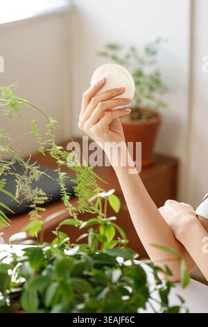 Le mani di una donna tengono in mano un panno bianco, rotondo e pulito per rimuovere il trucco in una stanza luminosa e ariosa. Foto Stock