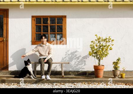 Un giovane uomo siede su una panchina con il suo cane in un giardino soleggiato. Foto Stock