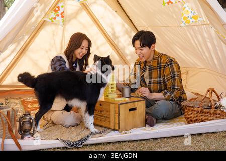 Una giovane coppia e il loro cane giocano a Jenga in un'accogliente tenda in un campeggio nella foresta. Foto Stock
