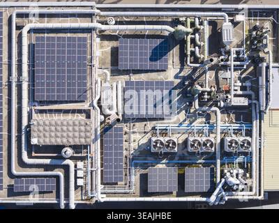Veduta aerea del tetto di un edificio industriale con pannelli solari, intricate reti di tubazioni e unità di ventilazione per il raffreddamento Taiwan. Foto Stock