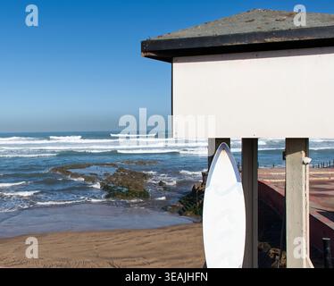 Insegna bianca in legno e tavola da surf con spazio fotocopie su una spiaggia soleggiata con onde oceaniche. Foto Stock